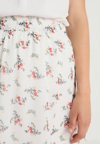 Floral skirt featuring a white fabric with small red and yellow flower patterns, an elastic waistband, and a lightweight, flowing texture.