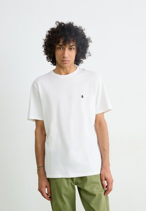 Witte katoenen t-shirt met een ronde hals, korte mouwen en een klein zwart druppellogo op de linkerborst. Gecombineerd met olijfgroene broek.