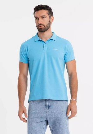 Polo de color azul claro con cuello, mangas cortas y un logo sutil. Presenta un corte relajado y una textura suave similar al algodón.