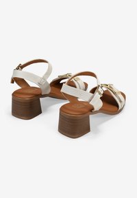 Sandalias de cuero blanco con tacones cuadrados, con correas ajustables y herrajes en tono dorado. Acabado texturizado en las correas, suelas marrones.
