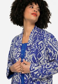 Langarm blouse met een blauw-wit abstract patroon, gemaakt van lichtgewicht stof. Kenmerkt zich door een sjawl kraag en knoopdetails.