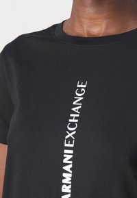 Czarna bawełniana koszulka z krótkim rękawem, z pionowym białym napisem "ARMANI EXCHANGE" na przodzie. Klasyczny okrągły dekolt.