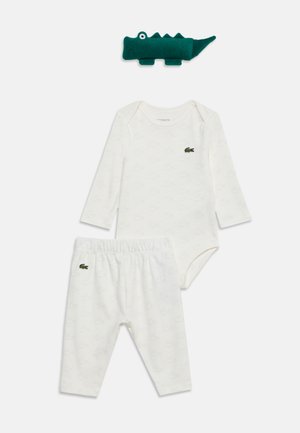 Ensemble body manches longues et pantalon pour bébé blanc avec des motifs subtils de crocodile et un petit logo crocodile vert, avec une peluche crocodile verte dessus.