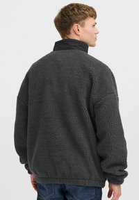Fleece jacket, gray, oversized fit, high collar with black accent, textured fabric, long sleeves, and ribbed hem.