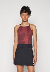 Crop top de sport rouge avec une texture, associé à une jupe noire avec une fente latérale et un détail de rayure blanche.