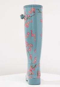 Botas de lluvia de goma azules con un acabado brillante, con un patrón floral rosa, acentos de ramas y una correa lateral para el ajuste.