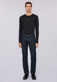 Camisa negra de manga larga con el logo "Trussardi"; pantalones de mezclilla azul oscuro con un corte clásico; zapatos negros pulidos; texturas suaves en todo el conjunto.