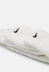 Valkoiset puuvillasukat, joissa on teksturoitu kangas, ja musta Nike-logo ommeltuna varteen. Muotoilu on uritettua ja pehmeää koskettaa.