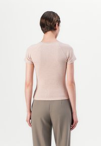 Light beige fitted short-sleeve top with a ribbed texture and raglan sleeves, paired with high-waisted beige trousers.