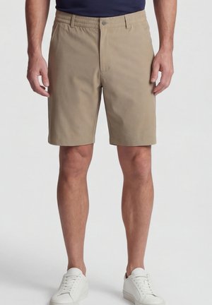 Beige men's knee-length shorts with elastic waistband worn with white sneakers and dark navy shirt against a plain background.