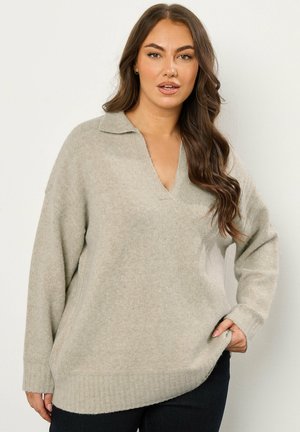 Pull en tricot gris clair avec un col en V, doté de longues manches, de poignets côtelés et d'un ourlet légèrement asymétrique.