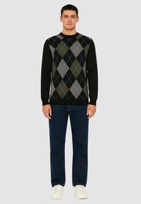 Maglione nero con motivo argyle verde, grigio e blu, scollatura rotonda e maniche lunghe, abbinato a jeans blu scuro e sneakers bianche.