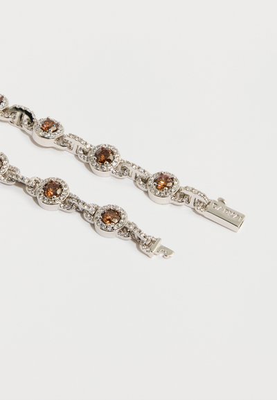 Srebrnasto zapestnico z okroglimi rjavimi dragimi kamni, obrobljenimi z majhnimi prosojnimi kamni. Ima obliko prepletenega verižnega vzorca in zaponko.