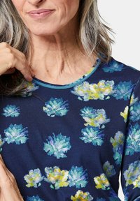 Marineblaues Langarmoberteil mit Rundhalsausschnitt, das ein florales Muster in Blau und Gelb aufweist. Leichte Stoff mit glatter Textur.