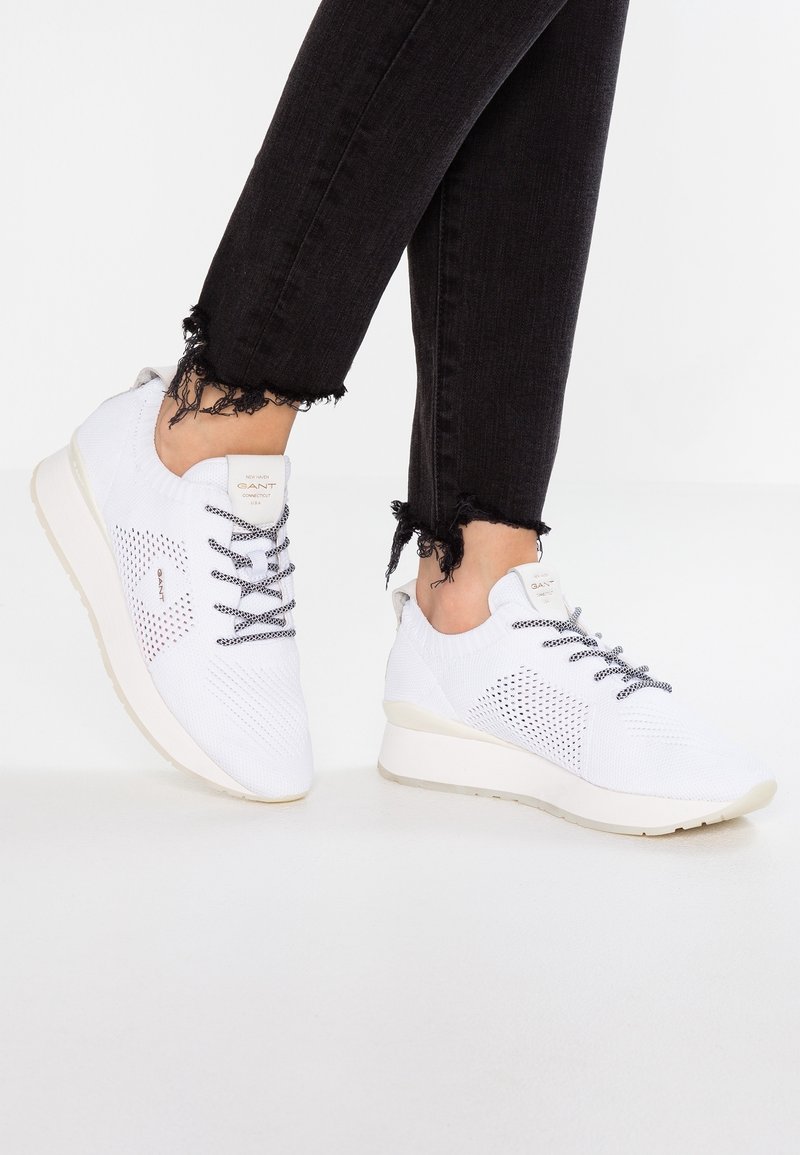 Baskets blanches tricotées avec un motif texturé, lacets à l'avant et une semelle légère. Portées avec un jean noir effiloché.