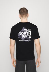 Černé bavlněné tričko s potiskem hory a textem "THE NORTH FACE NEKONČITĚ PROZKOUMÁVÁNÍ" na zadní straně.