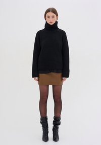 Maglione nero a collo alto in maglia, maniche lunghe, abbinato a una mini gonna in pelle marrone, collant neri trasparenti e stivali neri fino al ginocchio.