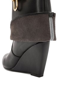 Botte à talon noir avec tige en cuir lisse, bracelet en daim à la cheville avec accent gris et détail en métal doré.