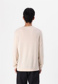 Bež pulover s dolgimi rokavi in okroglim izrezom, rebrastimi manšeti in robom; ima mehak teksturo in brezšivne ramena.