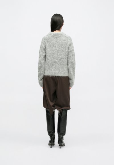 Grijze zachte trui met een kraag, gecombineerd met bruine wijde broek. Zwarte kniehoge laarzen maken de outfit compleet. Eenvoudig, gestructureerd ontwerp.