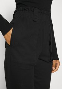 Černé cargo kalhoty s texturovanou látkou, mají elastický pas a boční kapsy. Detailní pohled na designové prvky.