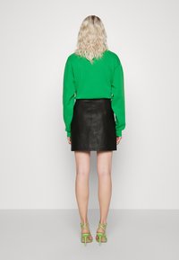 Felpa verde con maniche lunghe, abbinata a una mini gonna in pelle nera. Il portatore indossa tacchi verde a strappo e ha capelli biondi ondulati.