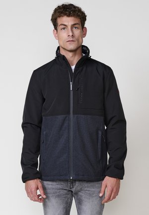 Chaqueta con cremallera en negro y azul oscuro que presenta un panel inferior texturizado, cuello alto, bolsillos laterales y detalle de logo en el pecho.