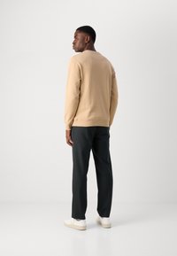 Sudadera beige con cuello redondo, combinada con pantalones oscuros y zapatillas blancas. Tejido suave con puños y dobladillo acanalados.