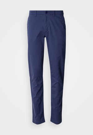 Στενά παντελόνια ανδρικά σε ναυτικό μπλε χρώμα με θηλιές για ζώνη, εμπρόσθιο κούμπωμα με κουμπιά, πλαϊνές τσέπες και ίσια μπατζάκια σε λευκό απλό φόντο.