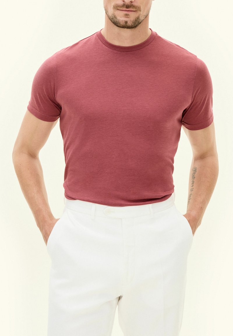 T-shirt rosso a maniche corte realizzato in tessuto morbido, con scollatura rotonda e design aderente. Abbinato a pantaloni bianchi sartoriali.