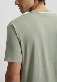 T-shirt di cotone verde chiaro con maniche corte, scollo rotondo e una sottile texture, arricchita da una cucitura decorativa sul retro del collo.