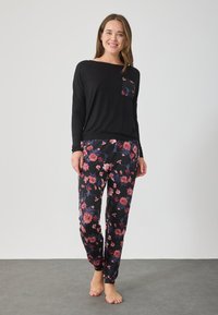 Μαύρη μπλούζα με μακριά μανίκια και λουλουδάτη τσέπη, συνδυασμένη με μαύρο παντελόνι με πολύχρωμο λουλουδάτο μοτίβο. Μαλακό ύφασμα, χαλαρή εφαρμογή και μανσέτες.