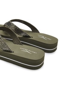 Grüne Flip-Flops mit strukturierten Riemen und glitzernden Akzenten, dicken Sohlen mit einem weißen Streifen und einem glatten Fußbett mit Branding.