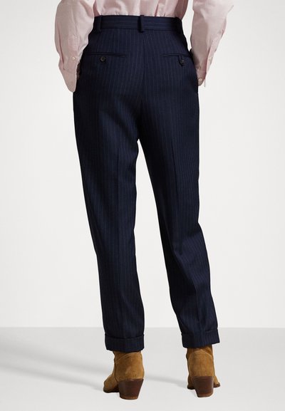 Navy pinstripe trousers with a tailored fit, featuring two back pockets, cuffed hems, and worn with tan suede ankle boots.