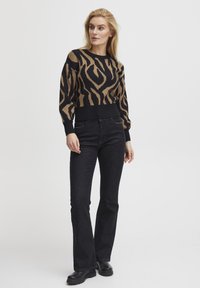 Črna in rjava zebra-linijska pletena pulover s rebrastimi manšetami in robom, v kombinaciji s črnimi širokimi kavbojkami in črnimi debelimi škornji.