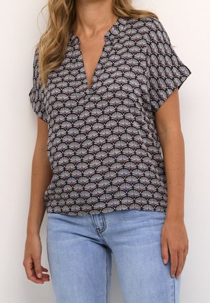 Kobieta nosząca bluzkę z krótkim rękawem i dekoltem w serek z czarno-lawendowym wzorem wachlarza, w połączeniu z jasnoniebieskimi dżinsami.