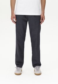 Pantaloni grigi scuri realizzati in tessuto strutturato, con design a gamba dritta, abbinati a sneakers grigie chiare e a una maglietta bianca semplice.