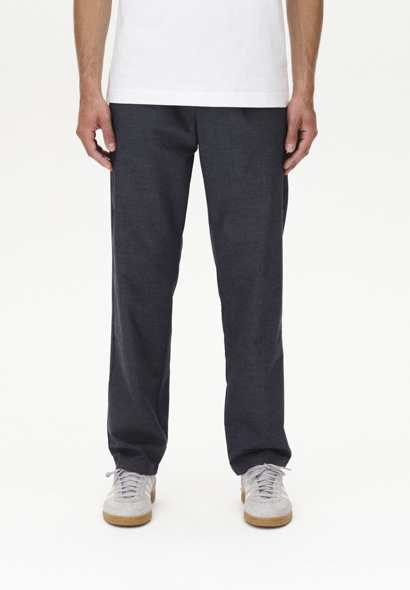Pantaloni grigi scuri realizzati in tessuto strutturato, con design a gamba dritta, abbinati a sneakers grigie chiare e a una maglietta bianca semplice.