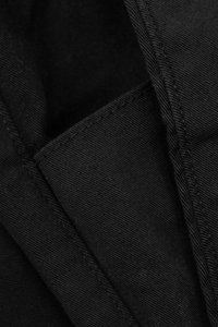 Tejido negro con una textura suave y costuras visibles. El material parece ser una mezcla de algodón duradera, presentando un diseño simple y limpio.