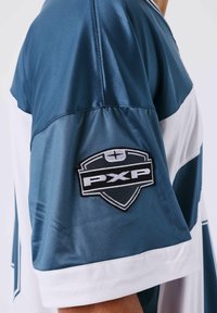 Camicia a maniche corte blu e bianca con una toppa logo scudo PXP in bianco e nero sulla parte superiore del braccio.