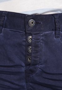 Marineblauwe katoenen broek met een vijfknopen flapsluiting met metalen accenten en zichtbare stiksels. Gladde textuur met een getailleerde pasvorm.