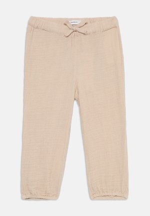 Pantalons légers beiges en tissu texturé. Dotés d'une taille élastique avec cordon de serrage et de poignets froncés au niveau des chevilles.