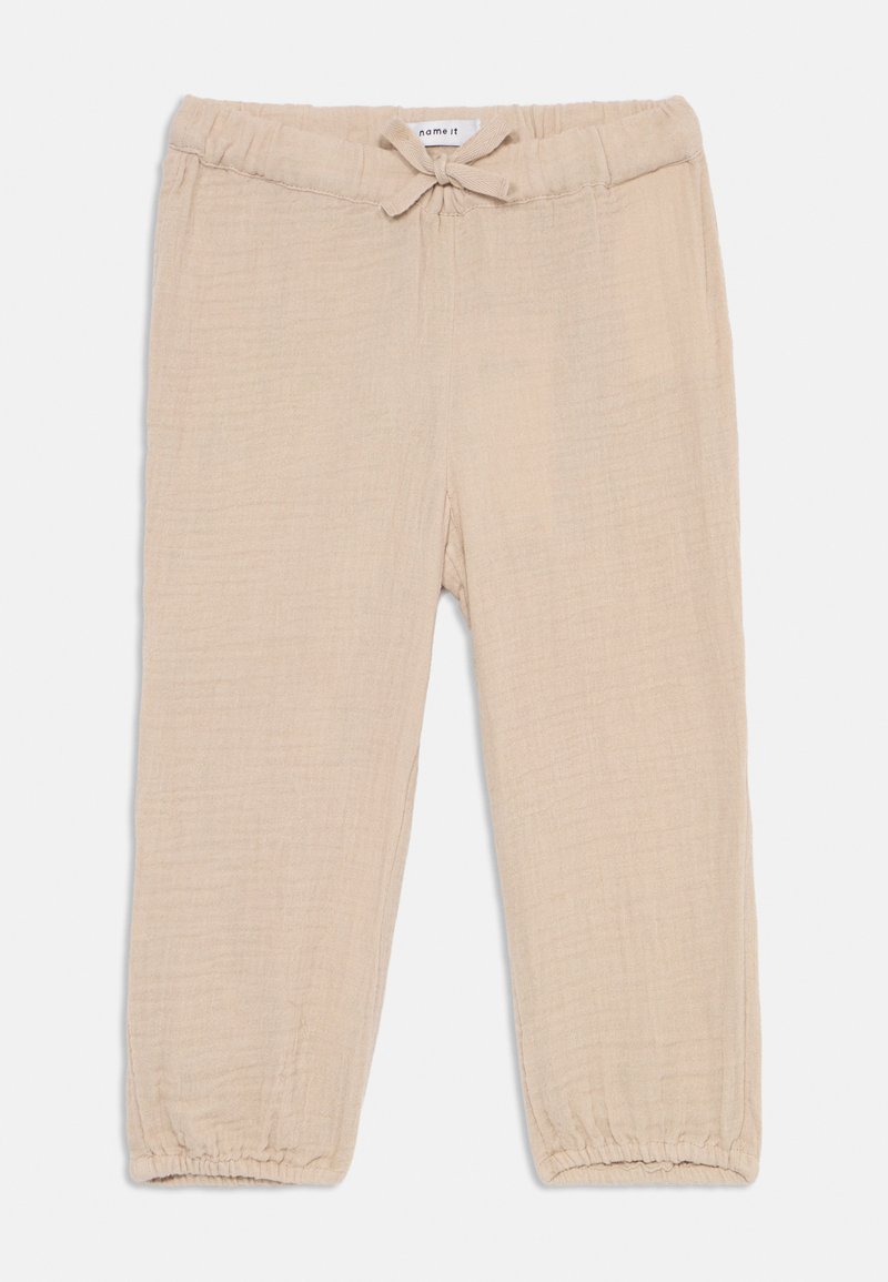 Beige, lette bukser med teksturert stoff. Har en elastisk midje med snor og rynkede mansjetter ved anklene.