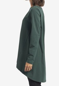 Tunic a maniche lunghe di colore verde scuro, realizzata in cotone morbido, con orlo curvo e vestibilità ampia, colletto rotondo e cuciture laterali.
