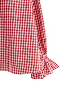 Red and white gingham fabric, featuring a gathered ruffle detail at the sleeve. Smooth texture with a checkered pattern throughout.