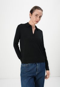 Zwarte pullovertrui met een kleine kraag, lange mouwen en een gestructureerde afwerking. Gecombineerd met losse blauwe denim jeans.