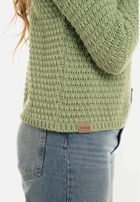 Lichtgroene gebreide trui met een textuurpatroon en een geribbelde zoom, voorzien van een klein, rechthoekig "Knit Factory" label aan de onderkant.