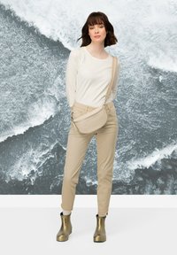 Beige kabelka přes rameno s texturovaným povrchem a zipovým uzavřením. Nosit s bílou košilí s dlouhým rukávem a hnědými kalhotami, doplněno kovovými botami.