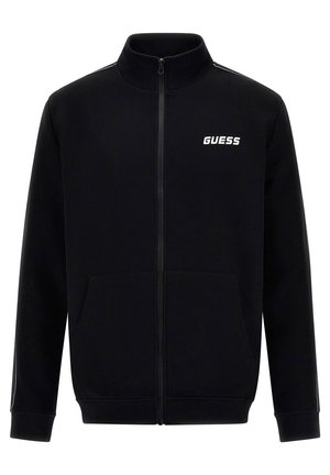 Chaqueta negra con cremallera, hecha de una tela suave, con dos bolsillos delanteros, un cuello alto y un logotipo blanco de "GUESS" en el pecho.