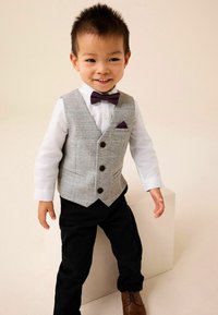 Szürke houndstooth mintaérmellény barna gombokkal egy fehér ing felett, fekete nadrággal és sötétlila masnival. Barna cipők egészítik ki az öltözetet.